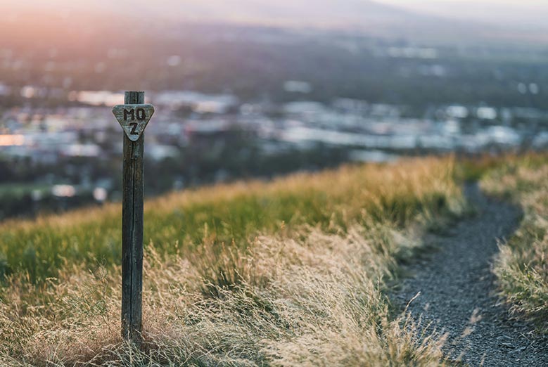 Walking down a trail looking at a sign and a blurred town of Missoula MT in the background